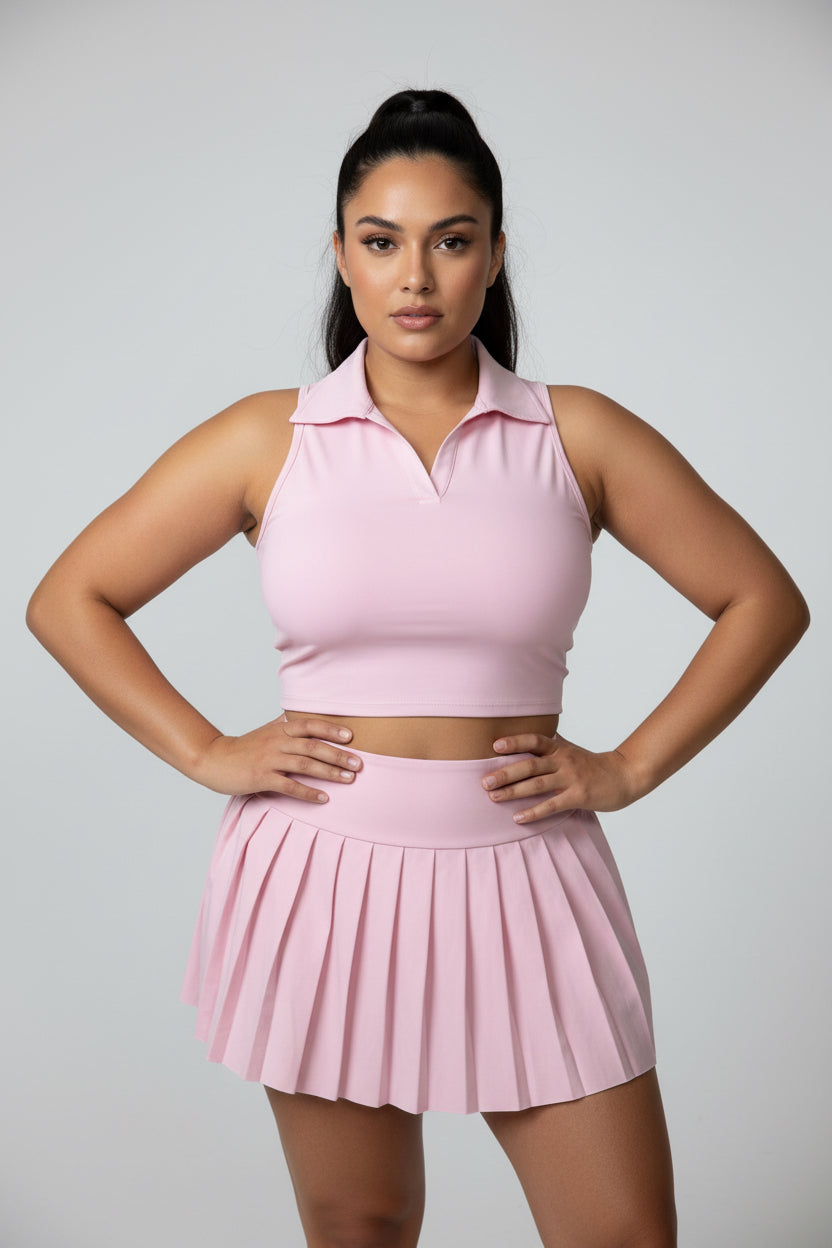 A pink two-piece athletic set consisting of a halter crop top and a matching pleated tennis skirt, Model is wearing Size small. 