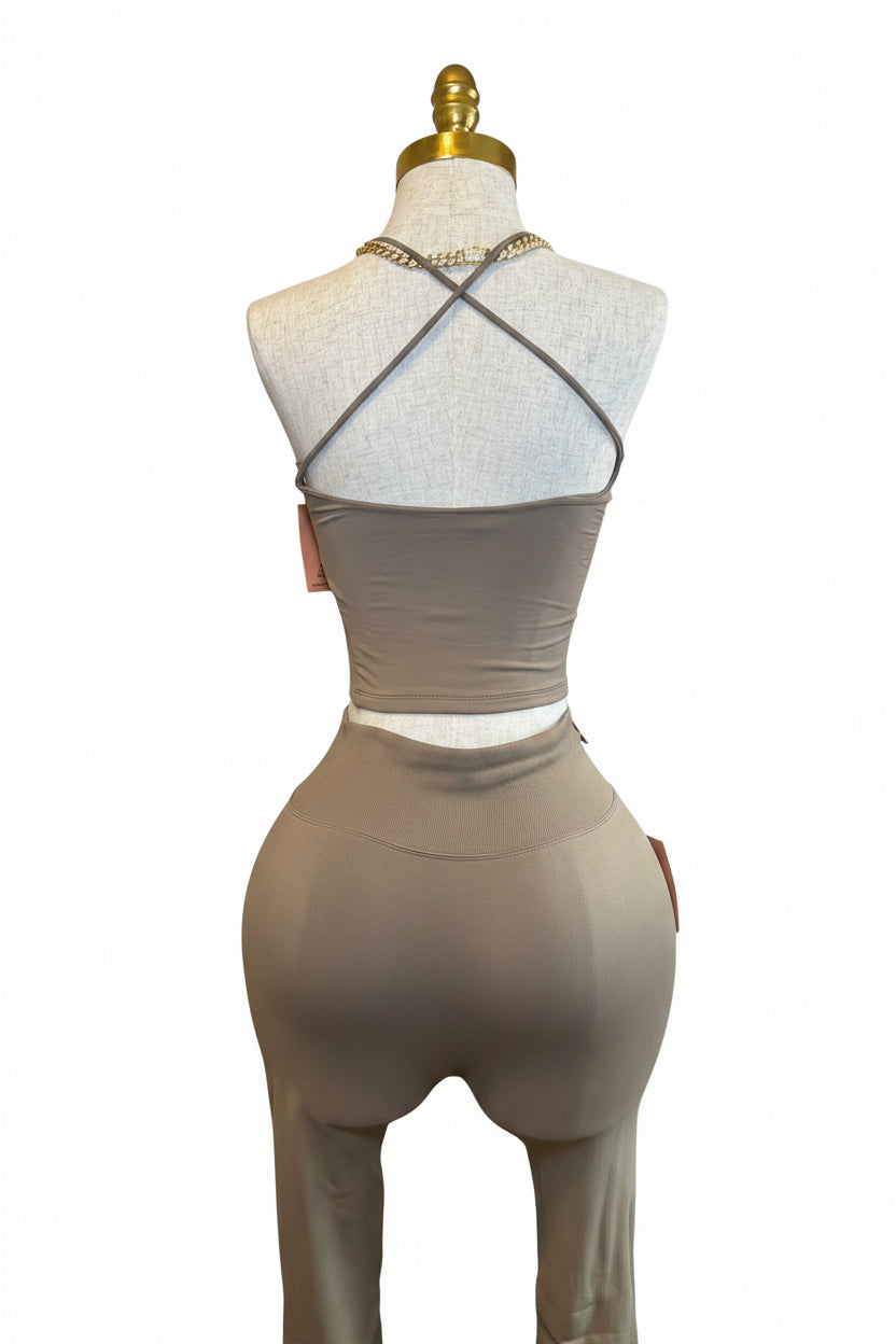 A beige two-piece activewear set consisting of a strappy crop top and matching high-waisted leggings, displayed on a white mannequin torso in a room setting.